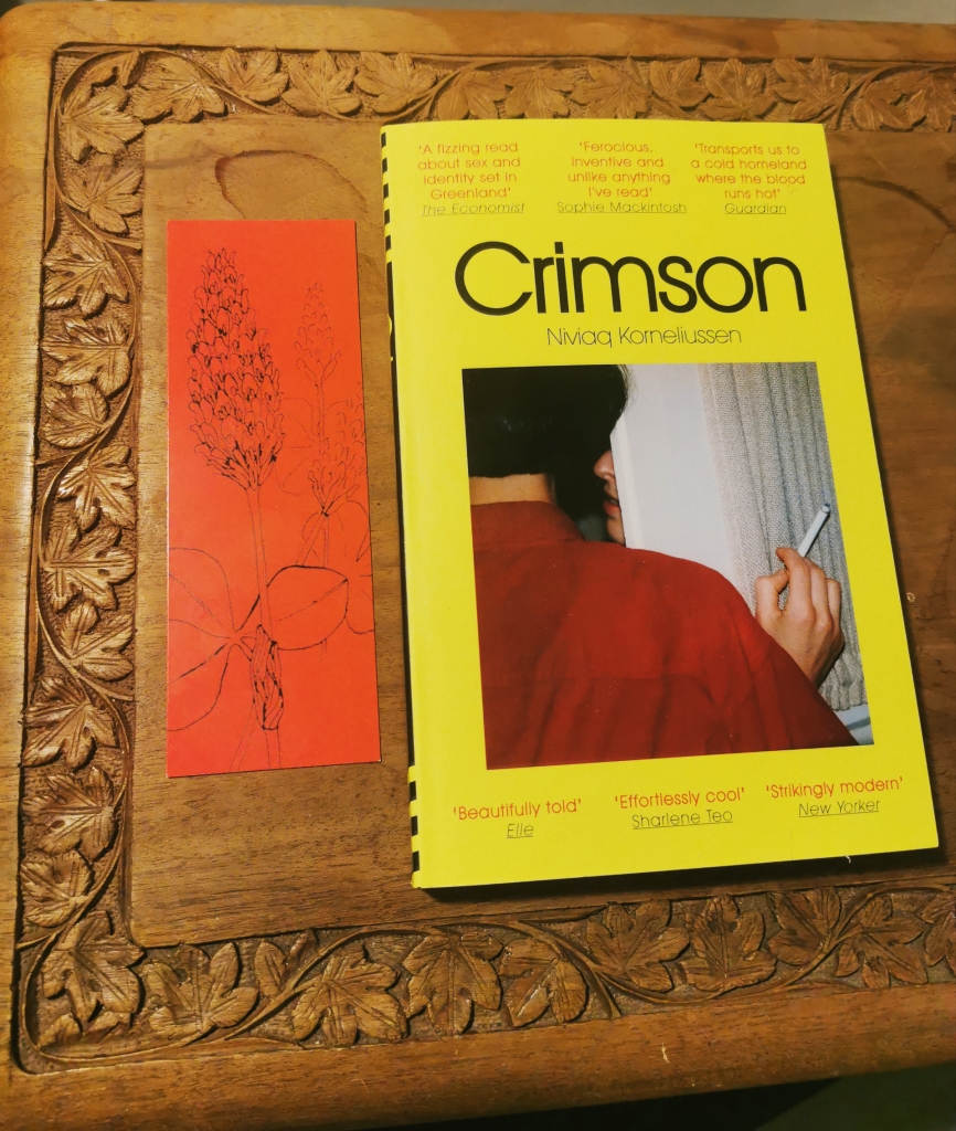 Photograph of a paperback copy of Crimson, with a themed bookmark.