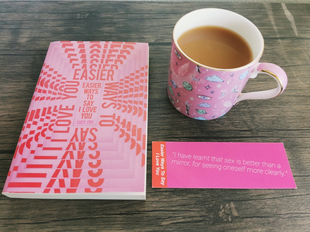 Photograph of a paperback copy of Easier Ways to Say I Love You, with a themed bookmark and a pink mug of tea.