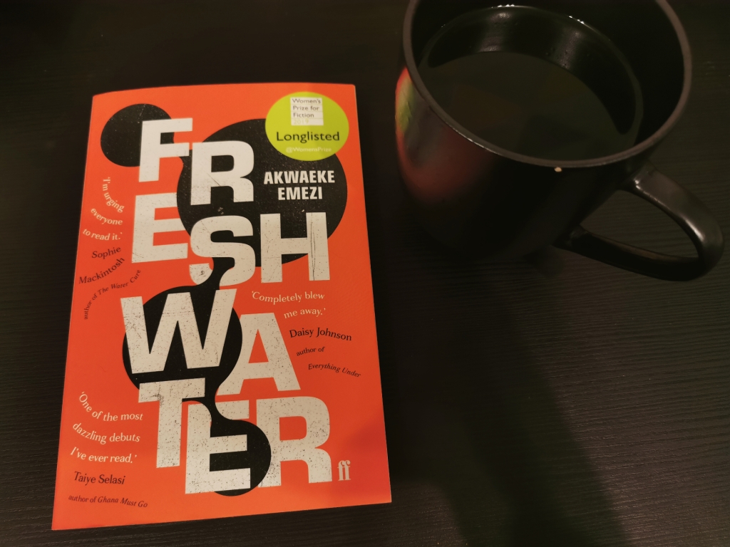 Photograph of a paperback copy of Freshwater on a black background with a black mug of black tea.